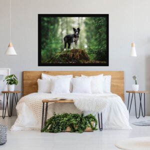 Minimalist bedroom featuring a wooden bed with white bedding, two bedside tables with plants, and a large framed photo of a dog standing on a mossy stump in the forest above the bed.